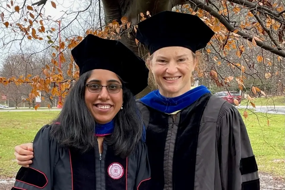 Graduate Shruthi Sriramkumar and Dr. O'Hagan pose in their graduation regalia outdoors on a fall day.