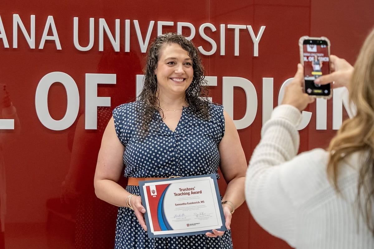 Samantha Evankovich smiles holding her award as someone takes her photo with a phone