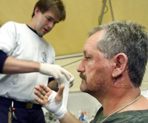 A young Dr. Strachan bandages a FEMA team member's hand. His patient has burns on his face.