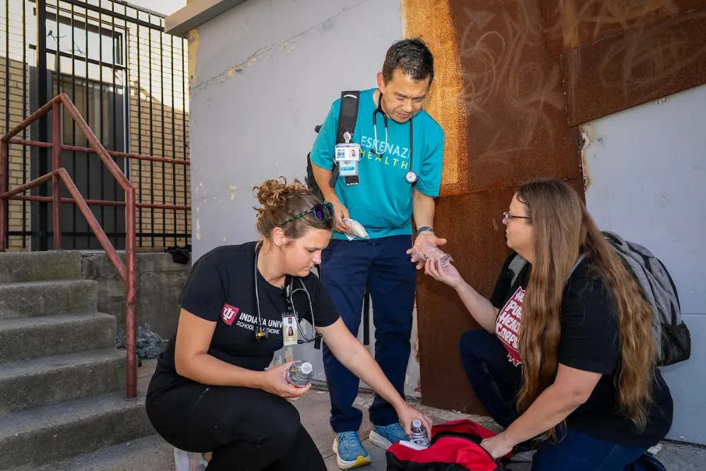 Mary Slaughter, Ira Means and Niki Messmore pull supplies out of a bag near an outdoor staircase and fence.