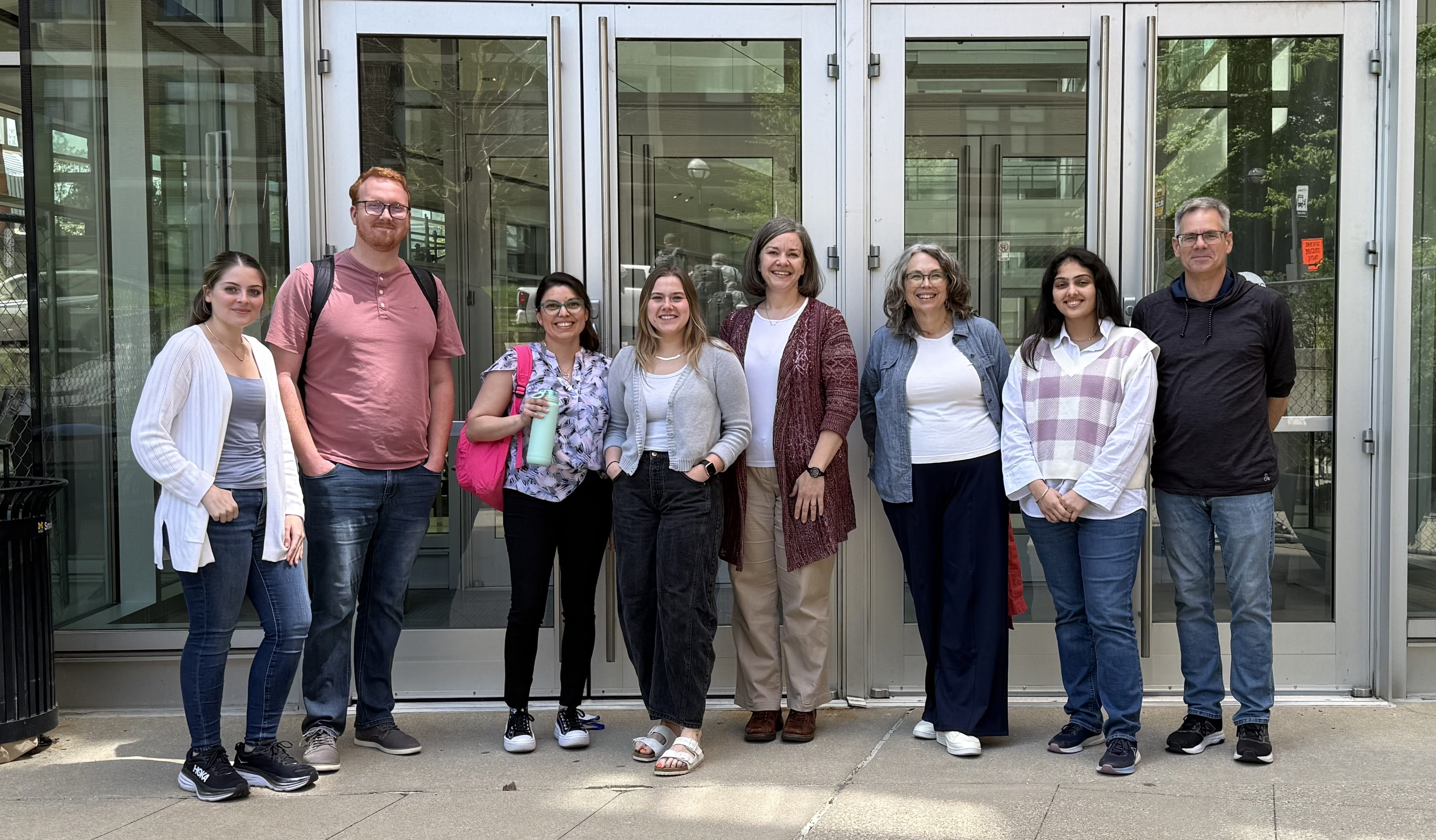 Eight members of the Turchi lab stand outside in front of doorways to a building