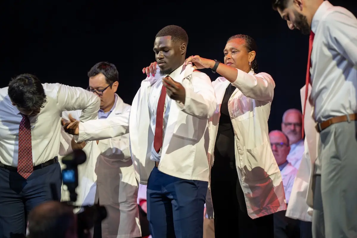 Mout-Maine Moustapha receives his white coat from a faculty member on stage during the IU School of Medicine White Coat Ceremony.