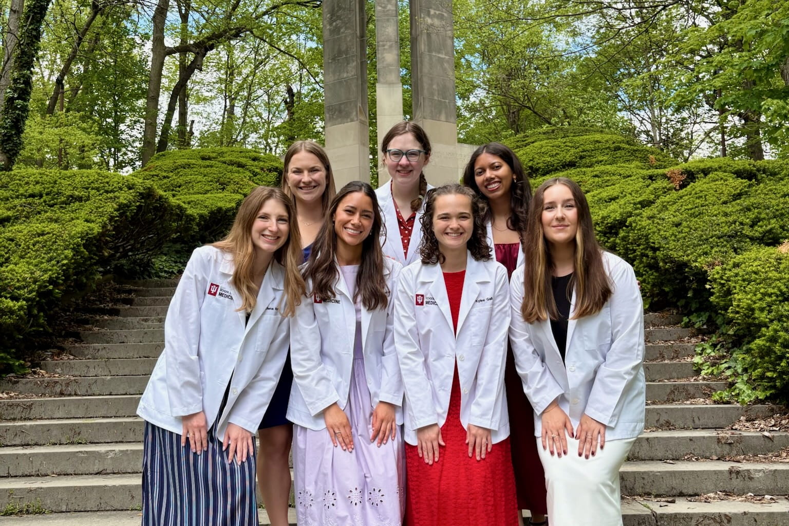 Seven female medical students pose outside wearing their white coats