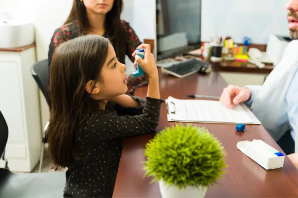 Young girl receiving asthma inhaler instructions from her doctor in an office setting.