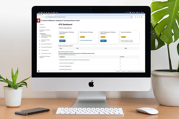 A Mac computer sits on a desk with a view of the ATS Scholars Portal dashboard on the screen.