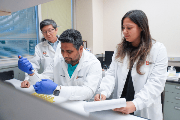 Zhour, Singh and Sharma in lab with white coats on looking at cells 