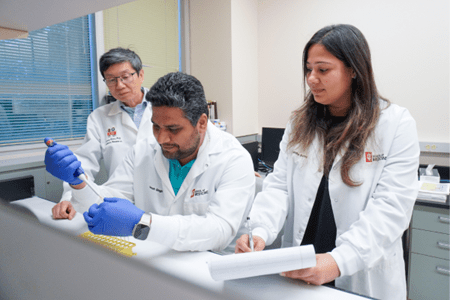 Zhour, Singh and Sharma in lab with white coats on looking at cells
