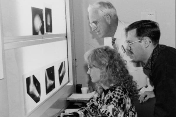 Dr. Klatte and colleagues leaning toward an x-ray imaging light box, in black and white.