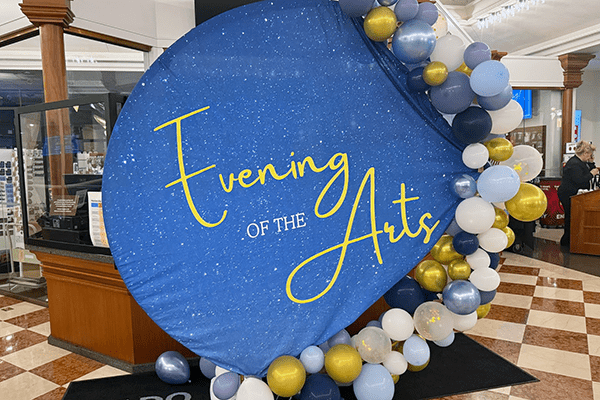 A sign next to balloons that says "Evening of the Arts" on it.