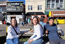 Three students from IU School of Medicine's Evansville campus pose for a photo while sitting at a table enjoying a meal at the 2024 West Side Nut Club Fall Festival.