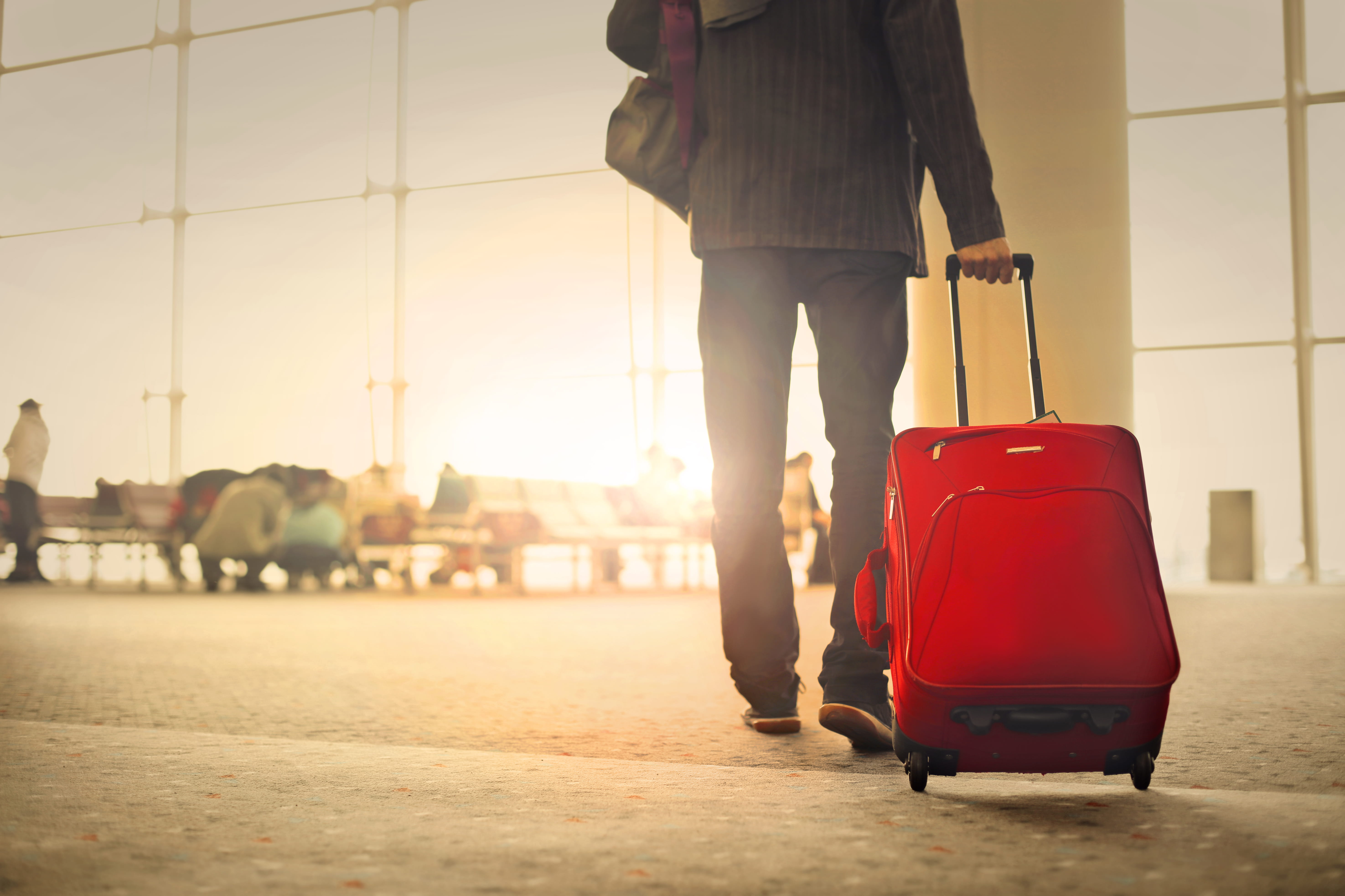 man pulling red luggage through airport 