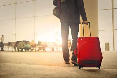 man pulling red luggage through airport
