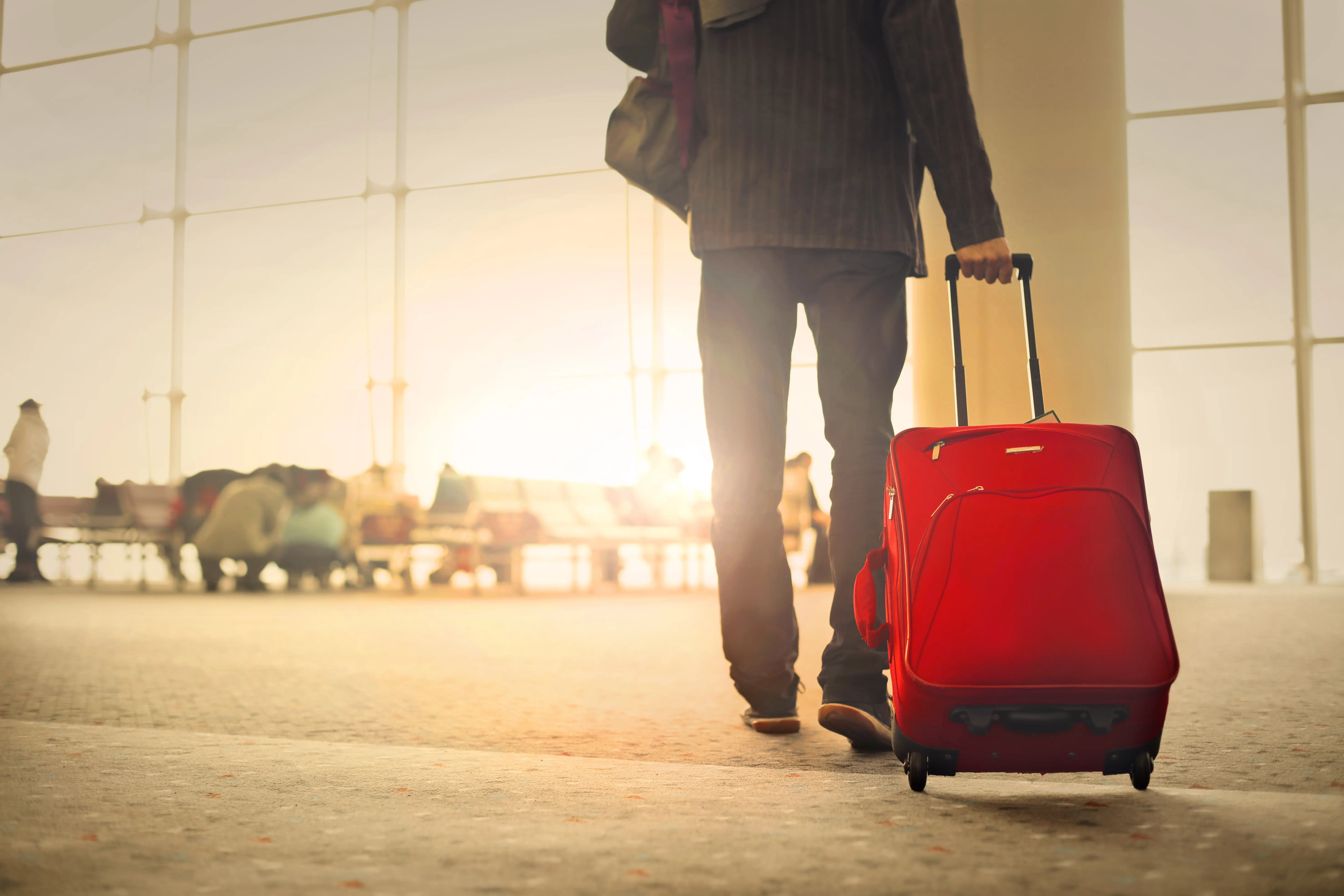 man pulling red luggage through airport 