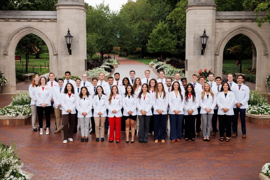 about 40 students in white coats in front of the sample gate in bloomington