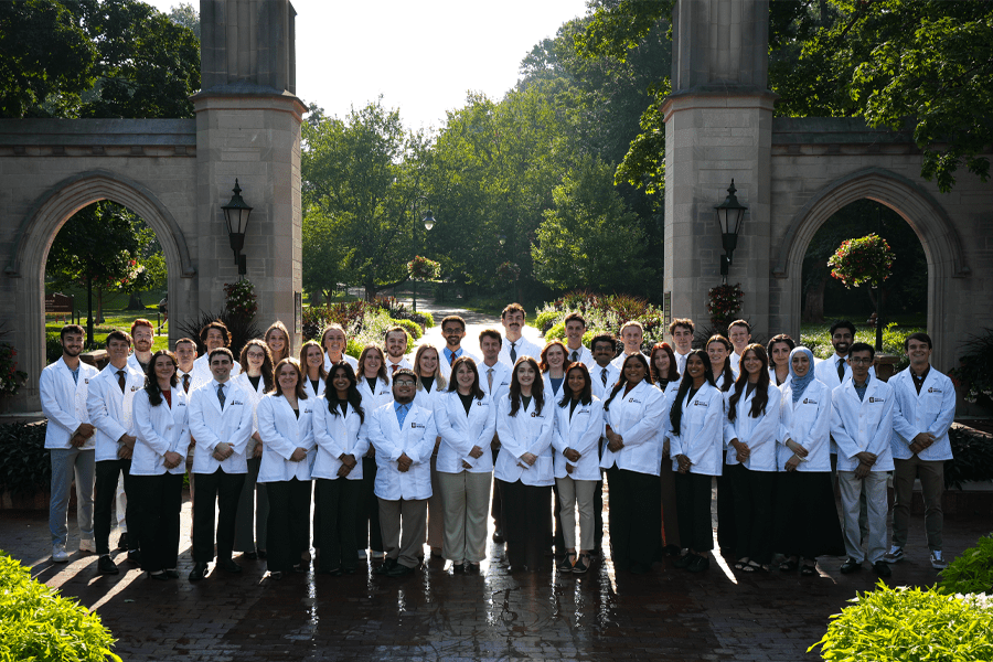 about 40 students in white coats in front of the sample gate in bloomington