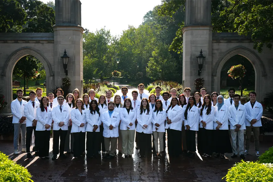 about 40 students in white coats in front of the sample gate in bloomington