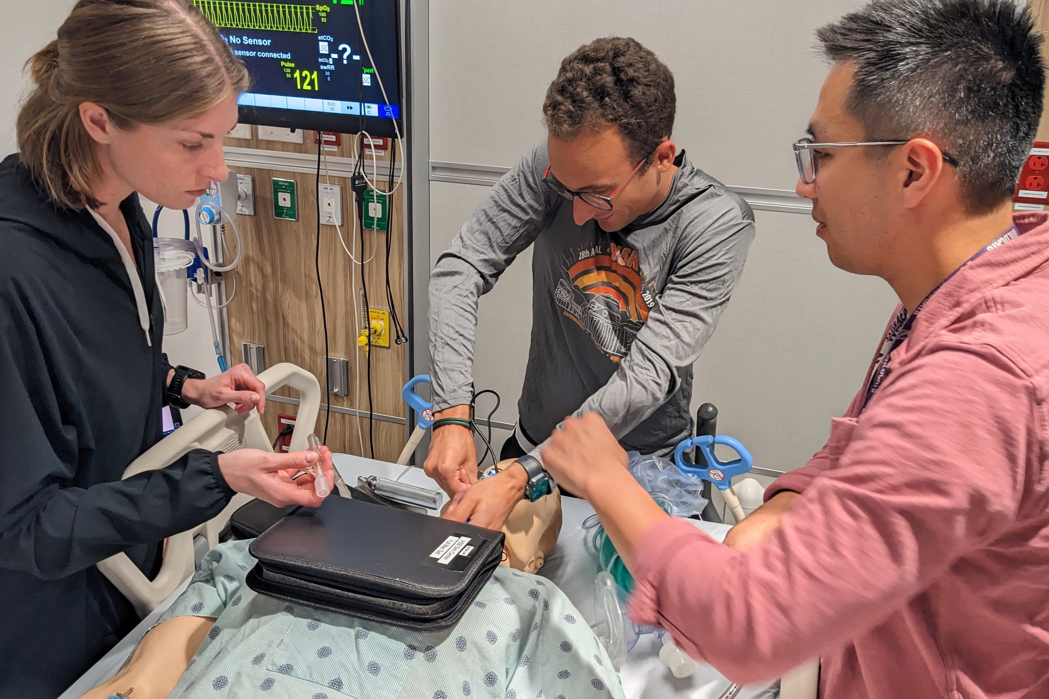 students work on a mannequin in a hospital bed in the sim center