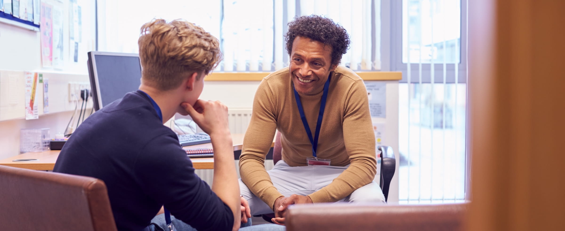a pyschiatrist smiles while speaking with a young patient in his office