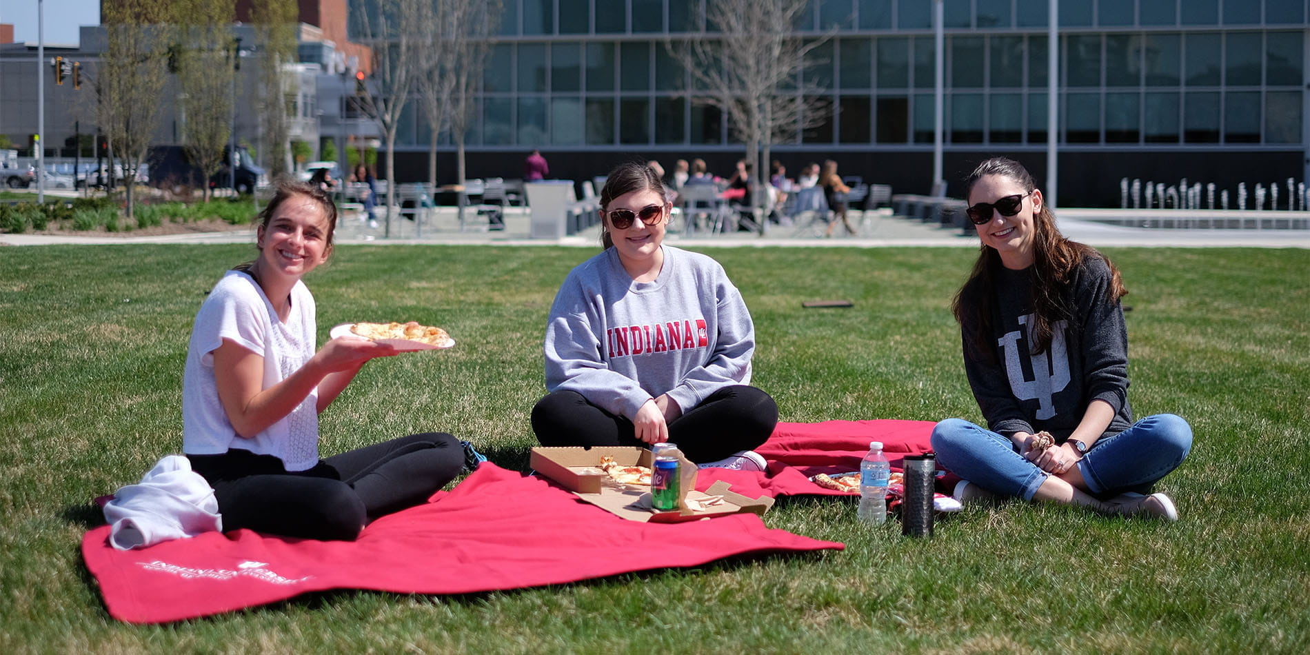 three students sit on the grass for a picnic outside on the Evansville campus