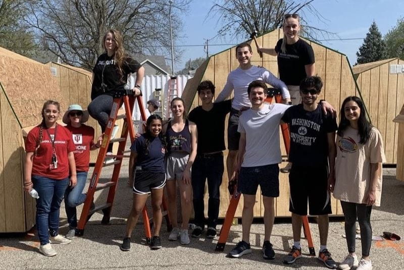 a large group of students stand in front of sheds they are painting with Habitat for Humanity