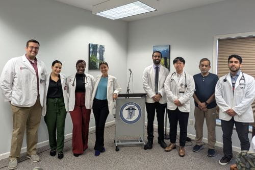 students in white coats surround a podium