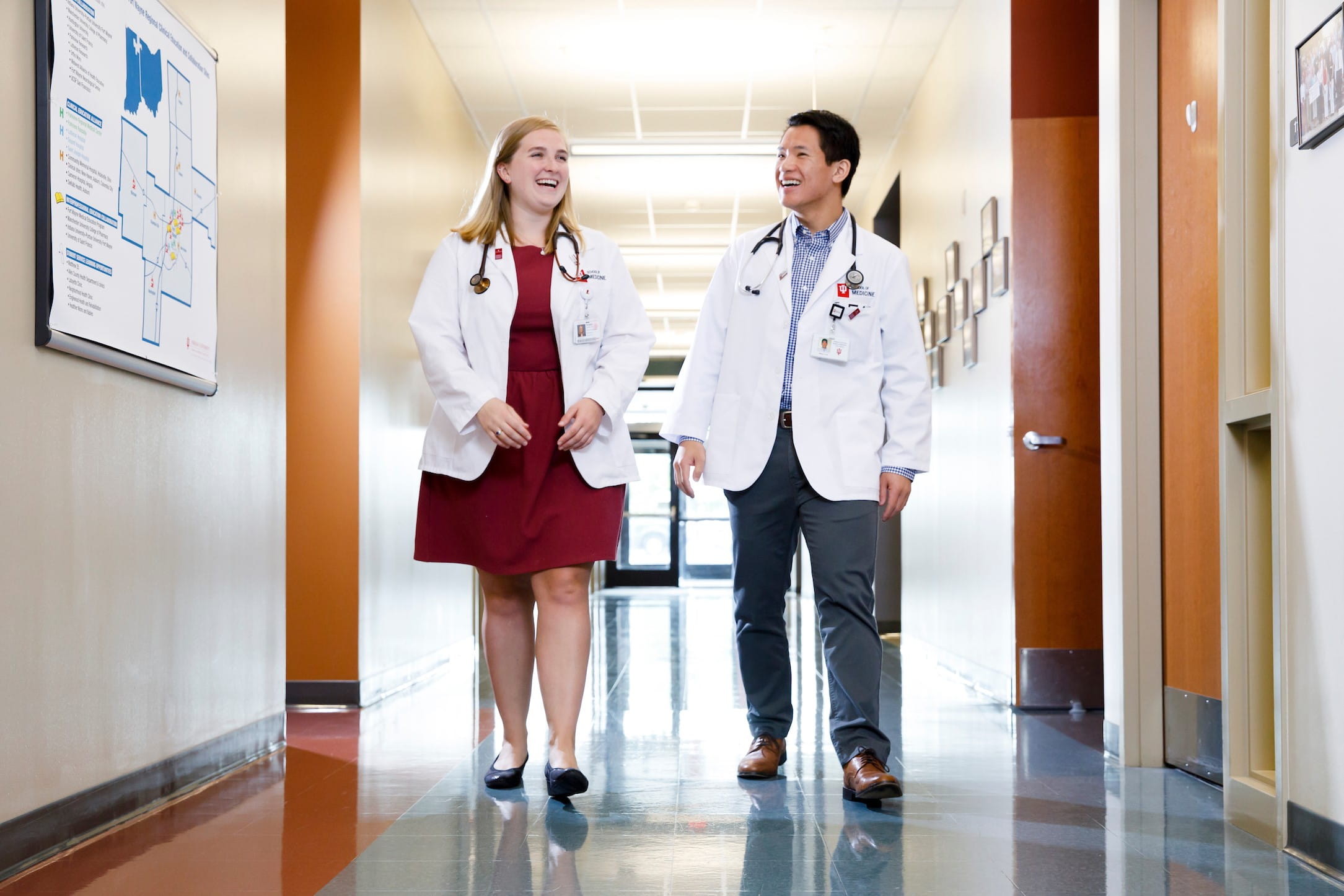 two students in white coats laugh and talk as they walk down a hallway in fort wayne