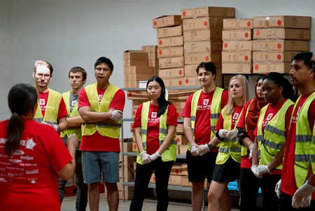 students in red t-shirts and yellow safety vests listen to instructions from a leader at the food bank in gary