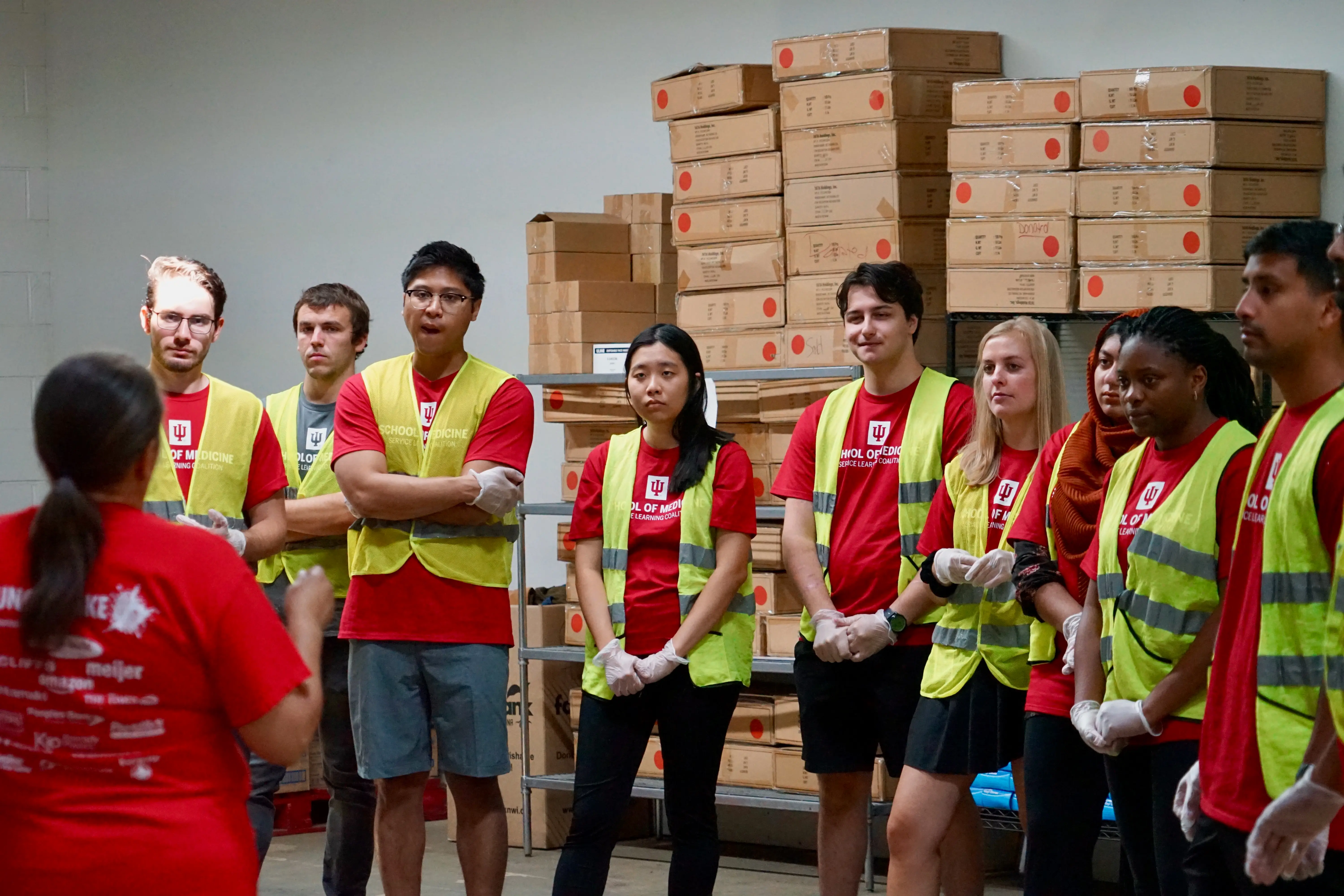 students in red t-shirts and yellow safety vests listen to instructions from a leader at the food bank in gary
