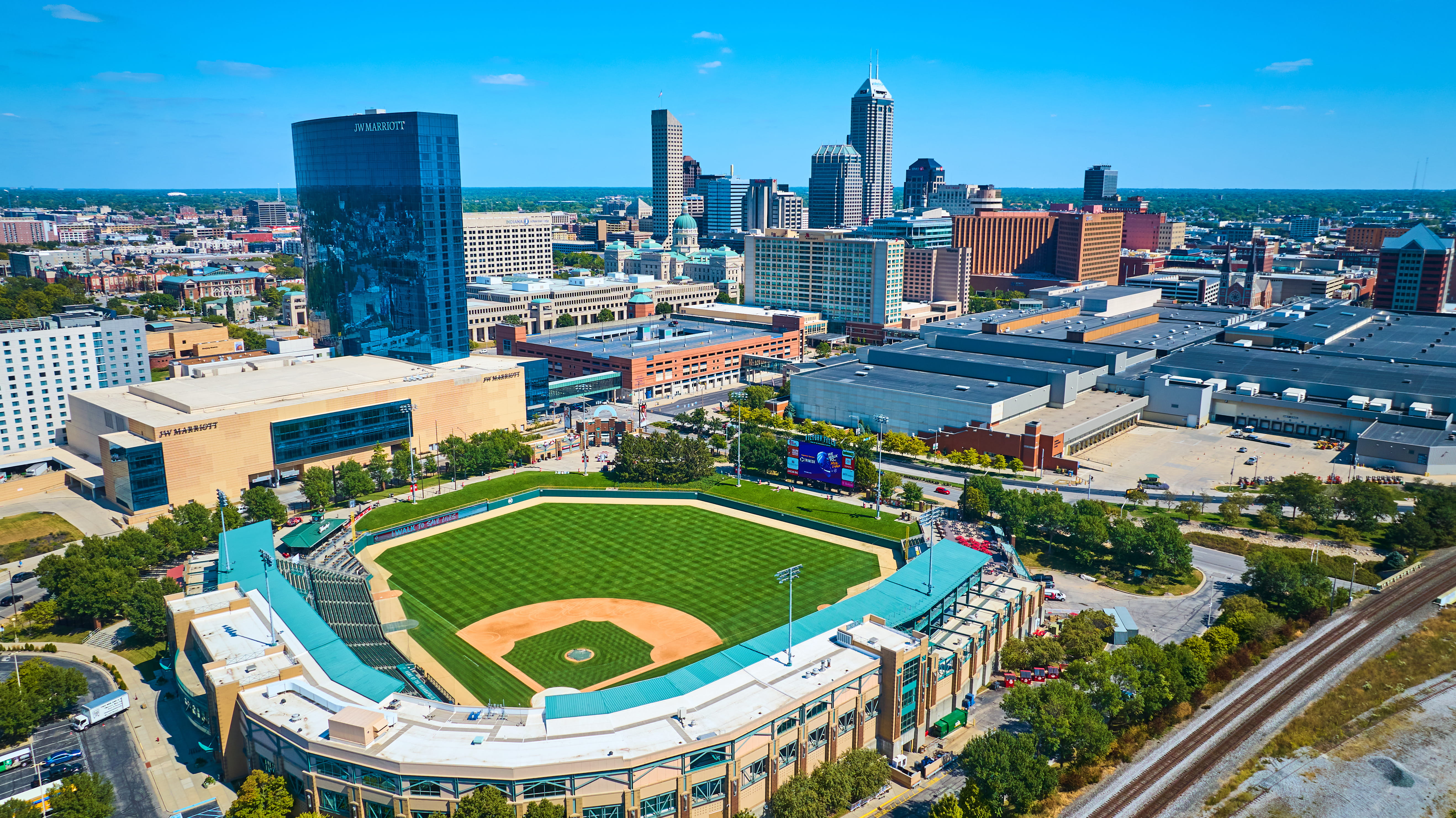 Aerial view of downtown Indianapolis with a baseball stadium in the foreground and city skyline behind it.