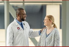 Doctor in white coat consoles patient outside clinic.
