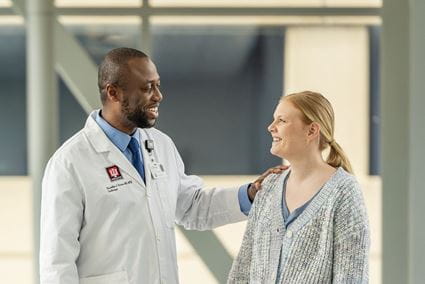 Doctor in white coat consoles patient outside clinic.