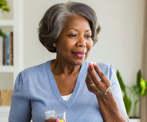 A mature black woman hold a pill in her hand before taking it. 