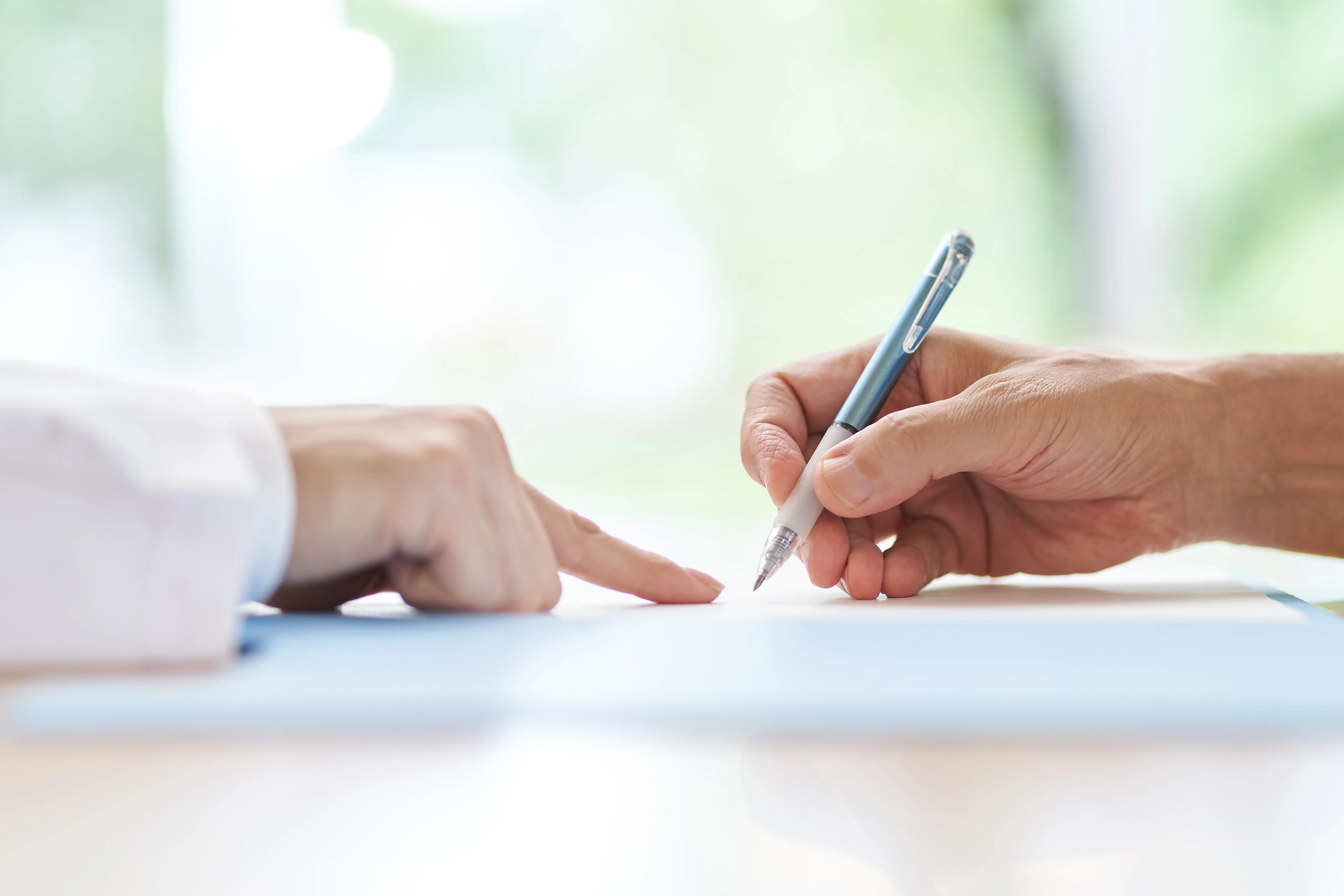 This illustrates a hand of a person signing a consent form while a health care professional's hand points to the paper. 