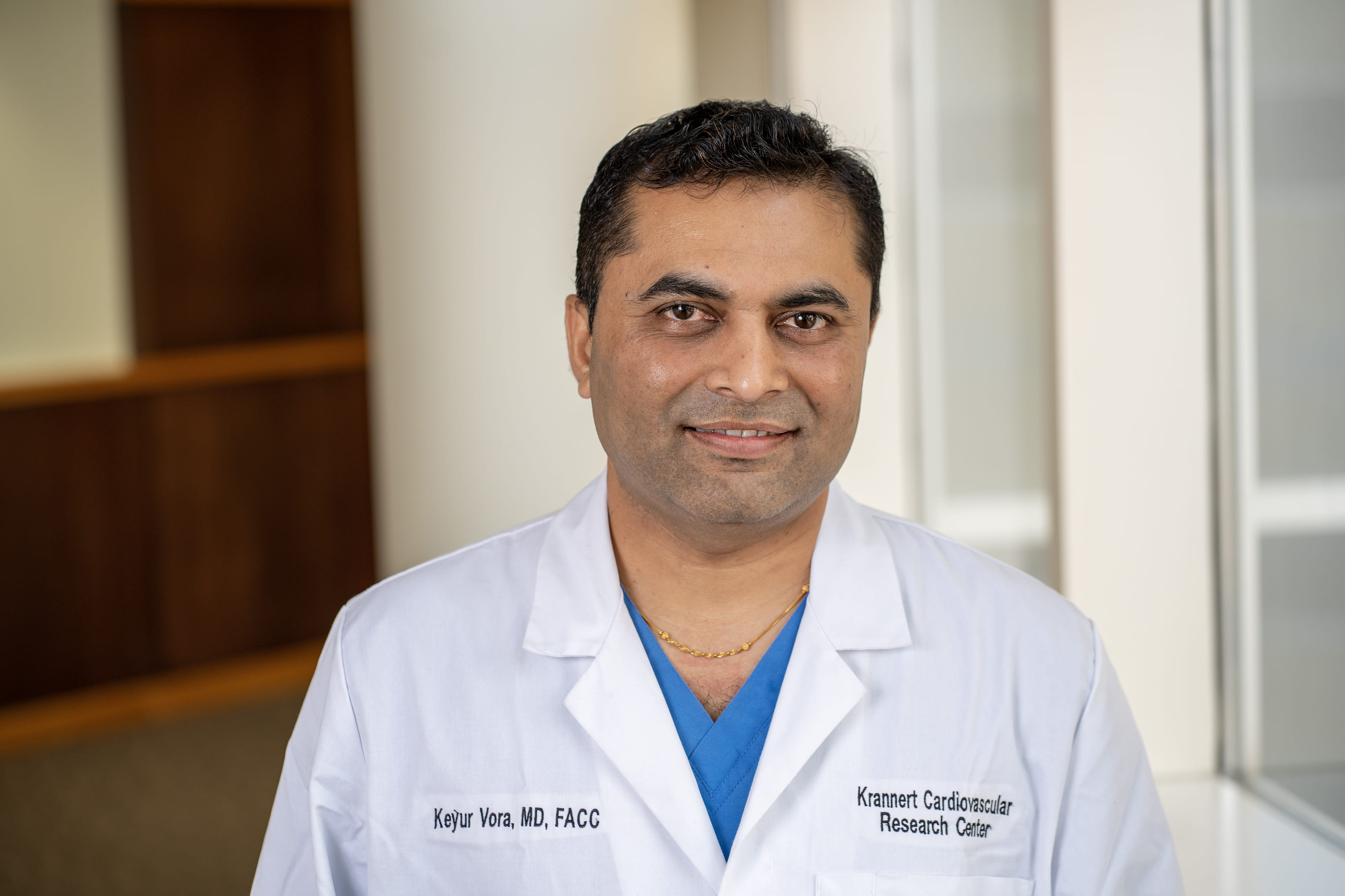 Keyur Vora, MD, shown from the chest up wearing a white lab coat with a blue shirt underneath.