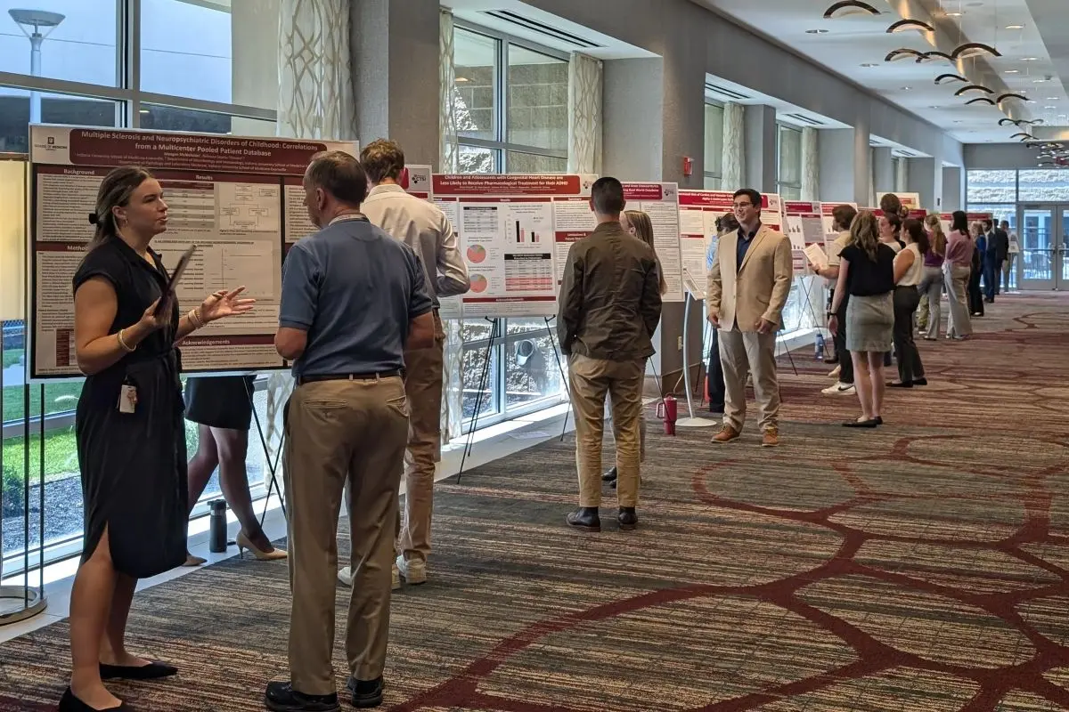 A long line of presenters standing in front of posters speak to other attendees at a scientific meeting