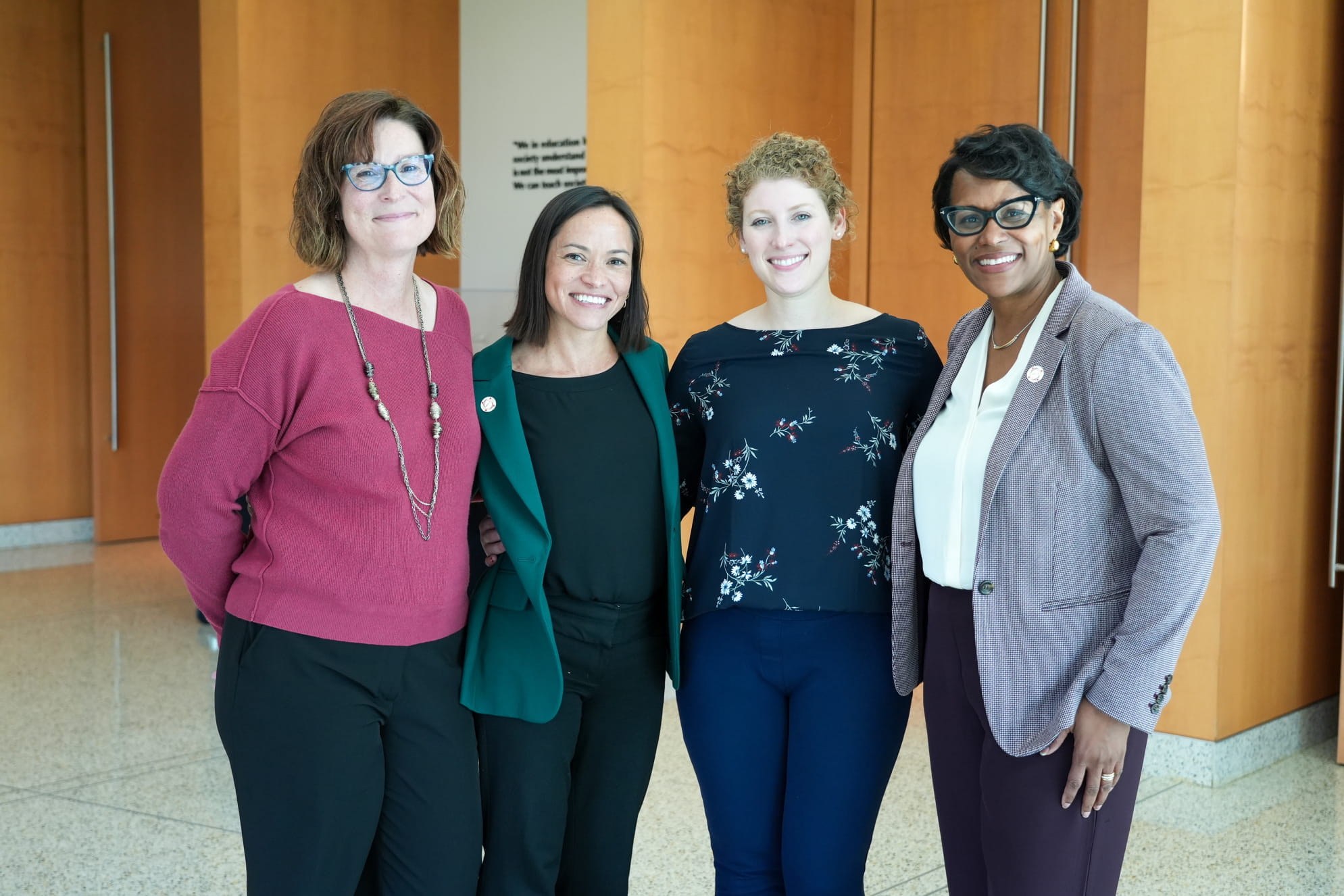 Four women standing together and smiling in a professional setting.
