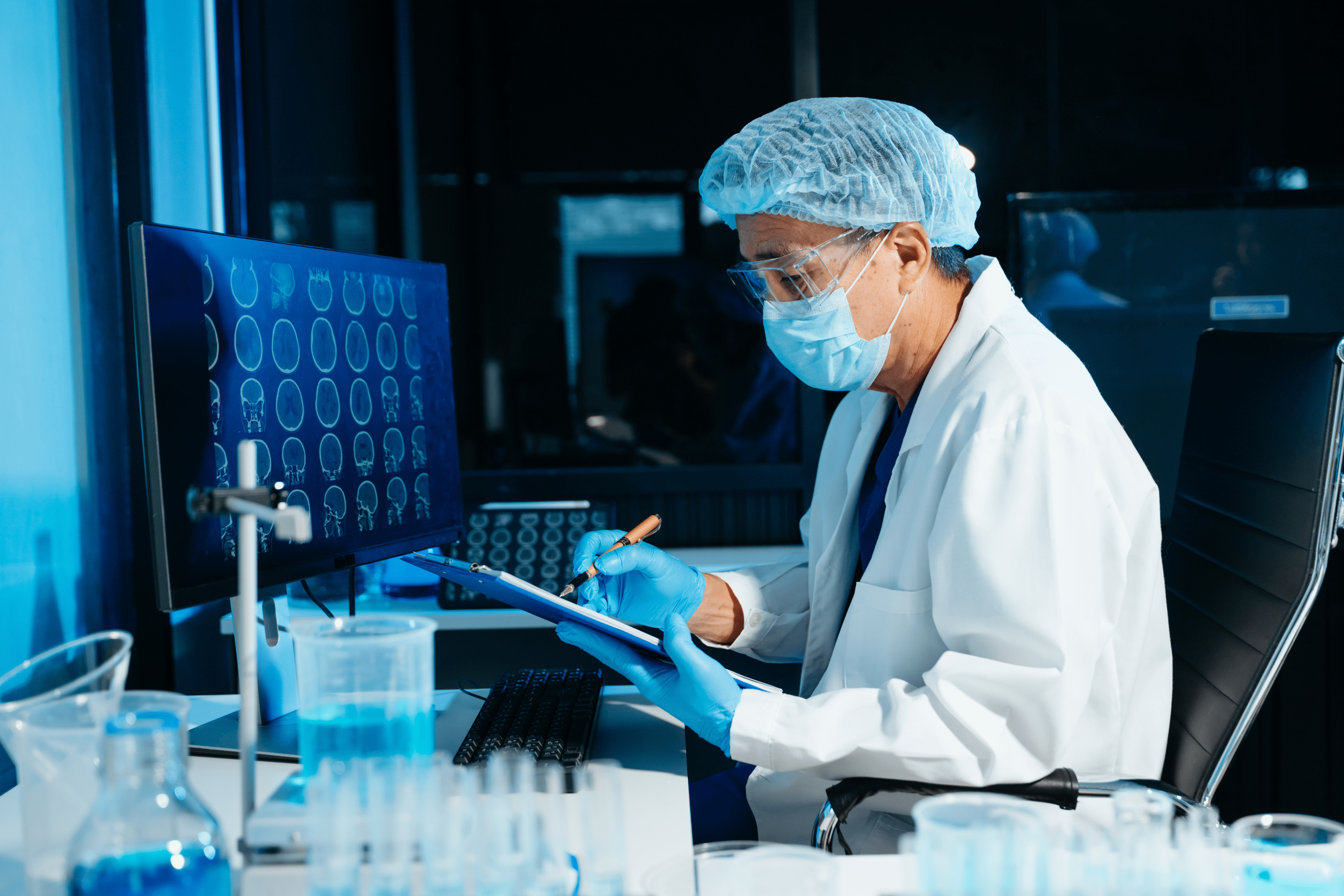 a researcher wearing protective head and face coverings reviews data on a clipboard in the lab