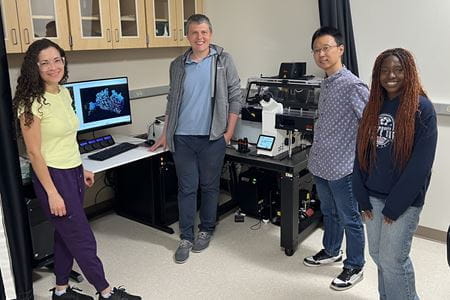 four members of the core team stand with equipment and computers behind them