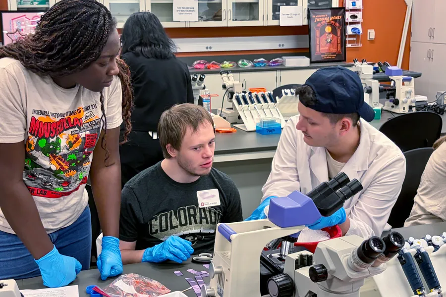 two graduate students work on a lab project with a person with down syndrome