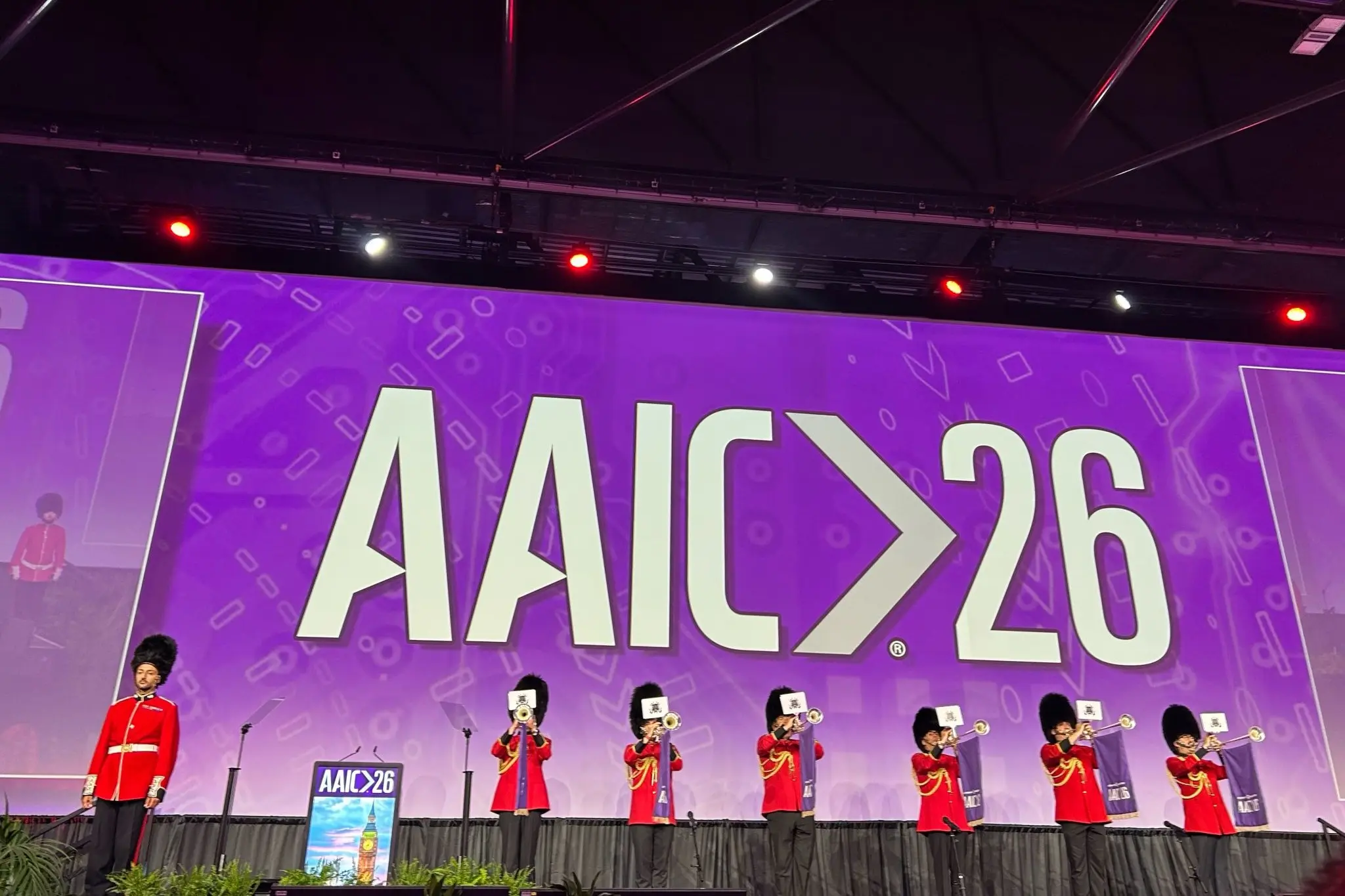 a line of the King's Guard stands in front of the AAIC 26 logo