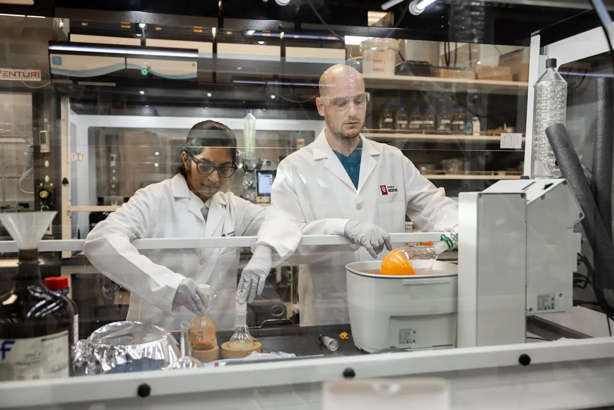 two researchers working in a lab behind glass