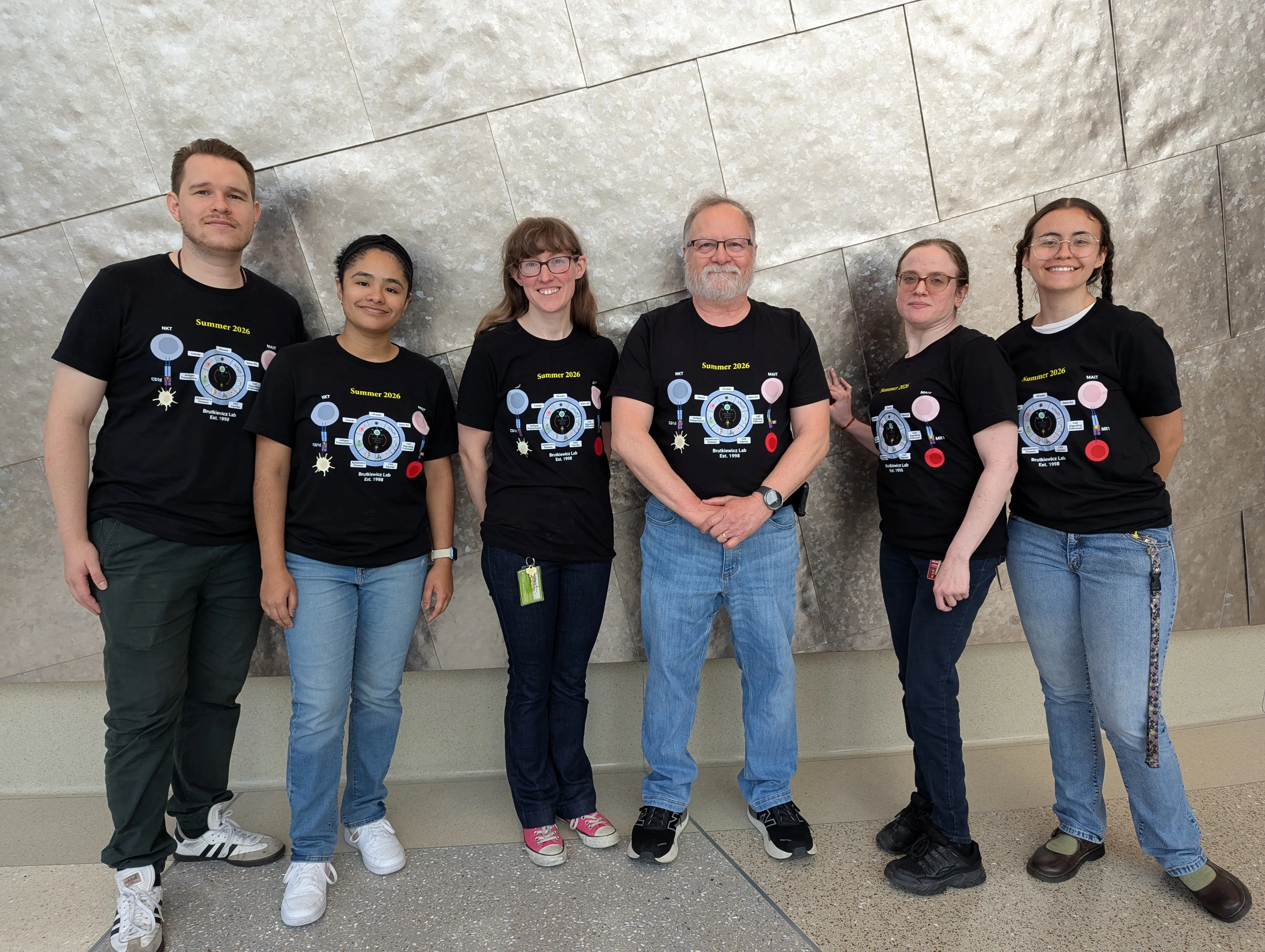 group photo of six people with matching shirts standing in front of a decorative wall