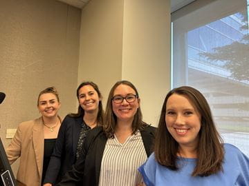 a group of women pose for a photo with a window behind them