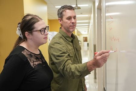 Two researchers use a white board in a hallway