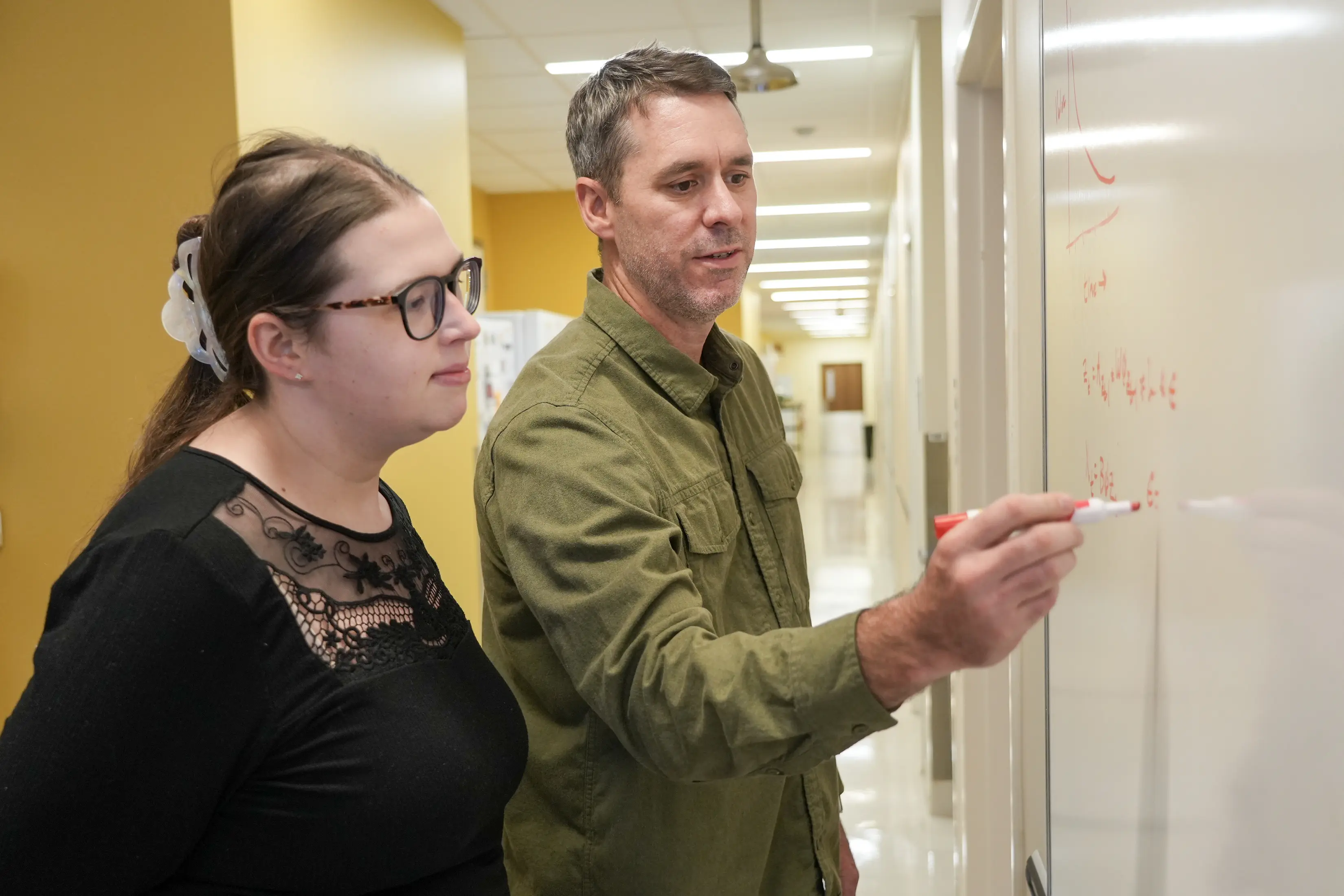 Two researchers use a white board in a hallway