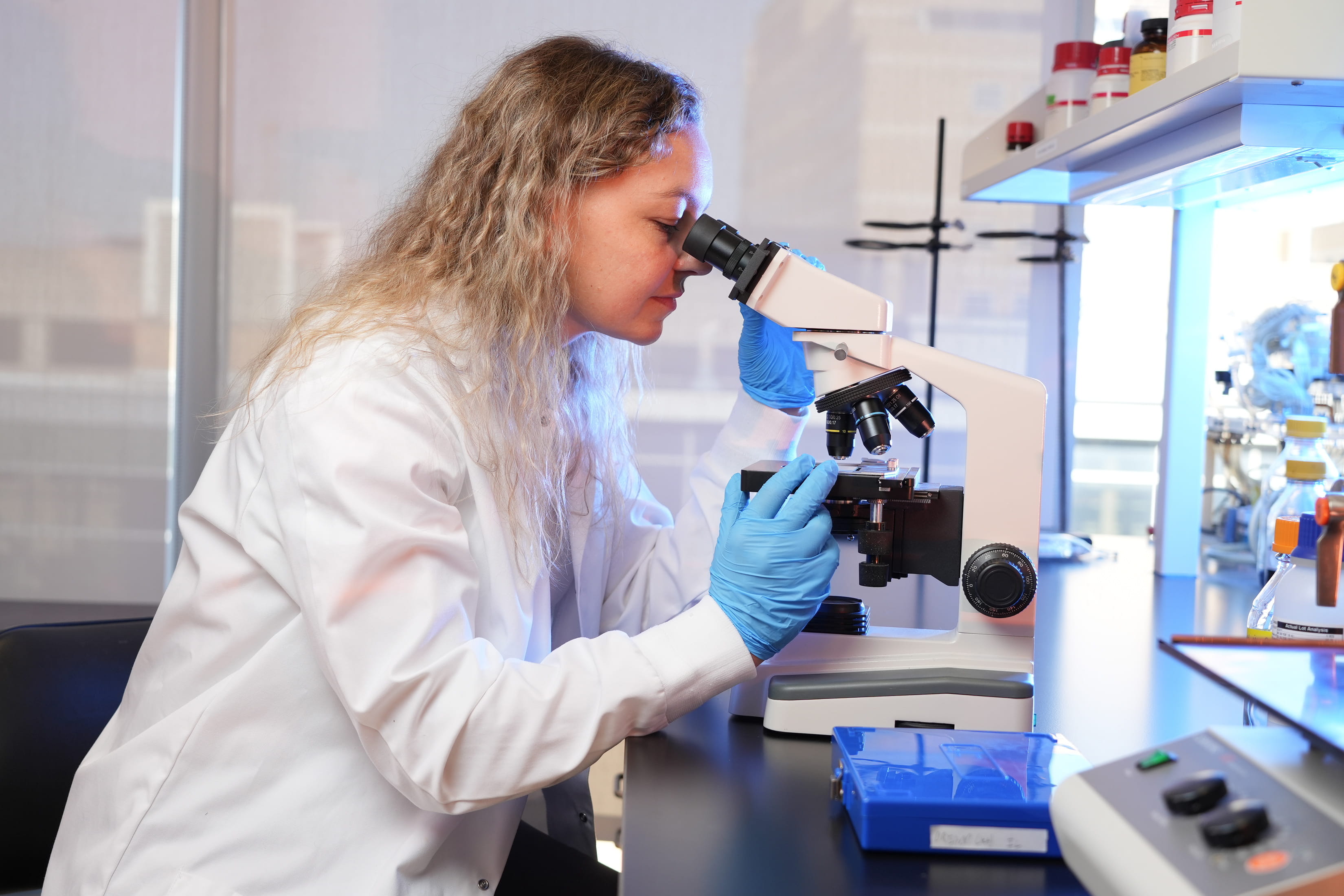 a graduate student looks into a microscope in a lab