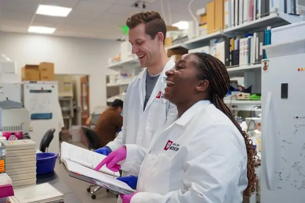 Matthew Austin and Rachael Morara smiling while looking over notes in the lab