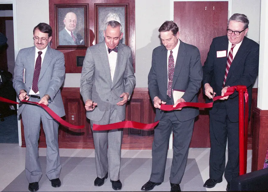 Four men in suits each cutting a section of a long red ribbon