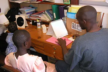 A girl sitting at a desk with a man working on a notepad