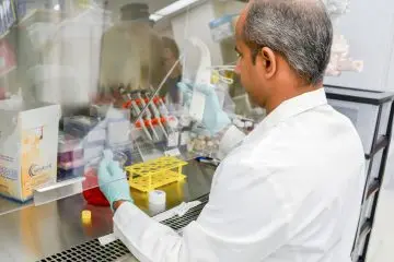 A man in a lab coat prepares a sample under the hood